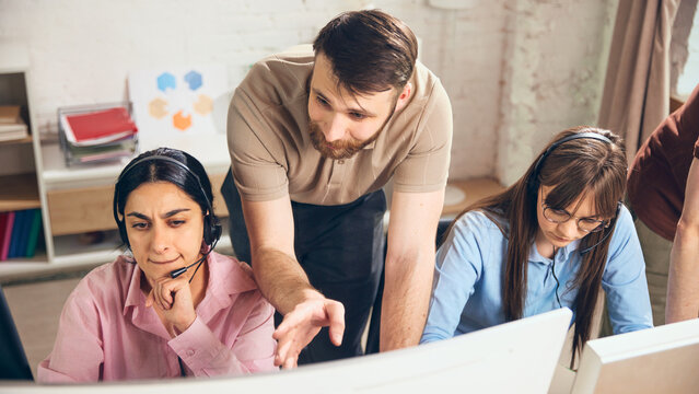 Support supervisor helping operators solve client request in office. Concept of customer service training, helpdesk supervision, client issue resolution, call center coaching, and team support.