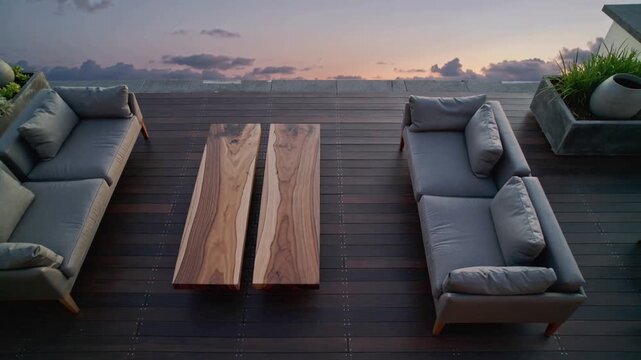 Deepening sunset sky casting soft shadows on rooftop deck, revealing grey sofas and wooden table