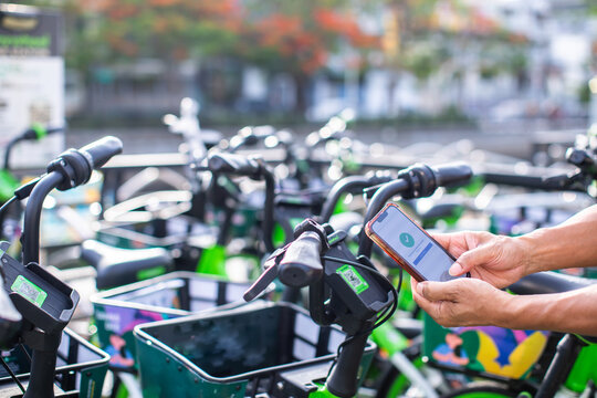 A close-up shot of hands holding a smartphone to scan a QR code on a blue shared bicycle's handlebars, unlocking it for a ride on a blurred city street.