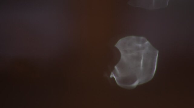 an abstract shot of light refracting through water drops flowing down a window pane during a rainy night with selective focus creating a blurry moody background texture