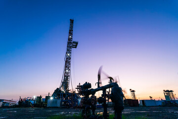 Obraz premium in the evening, oil pumps are running, The oil pump and the beautiful sunset reflected in the water, the silhouette of the beam pumping unit in the evening.