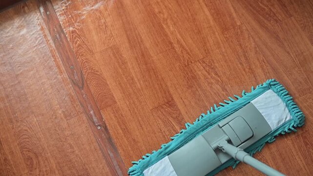 A mop moves across a wooden floor, removing dirt and dust in a systematic manner. The action demonstrates effective cleaning practices suitable for home maintenance