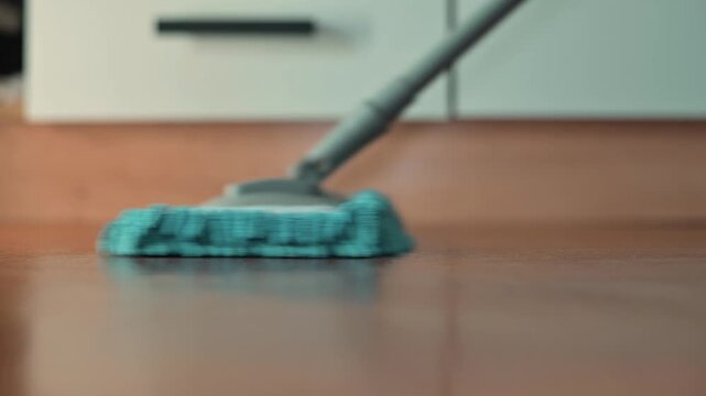 A person is mopping the floor in a well-lit indoor space using a blue mop. The action focuses on maintaining cleanliness and organization within the home