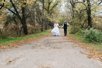 Fototapeta premium bride and groom walking along a path in an autumn forest