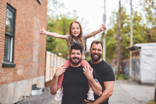 A Portrait of a happy gay couple outdoors in urban background with his adopt little girl
