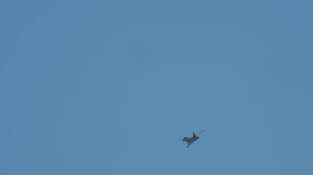 A modern delta-wing fighter jet performing a high-speed aerial maneuver against a clear cloudless blue sky, appearing small against the vast atmosphere