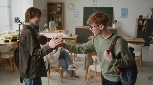 Teenage boys doing their special friend handshake after meeting during 3D modeling class in modern school