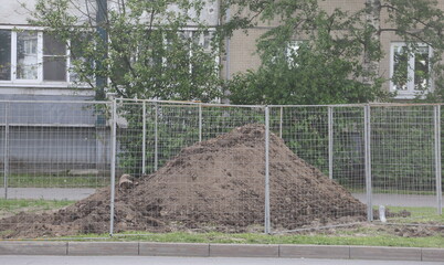 Fototapeta premium A pile of soil dug up on the lawn is surrounded by a chain-link fence