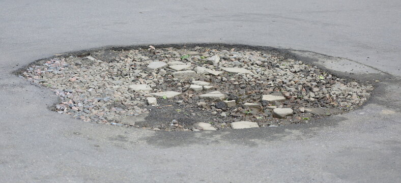 A large pothole in the asphalt pavement filled with crushed stone