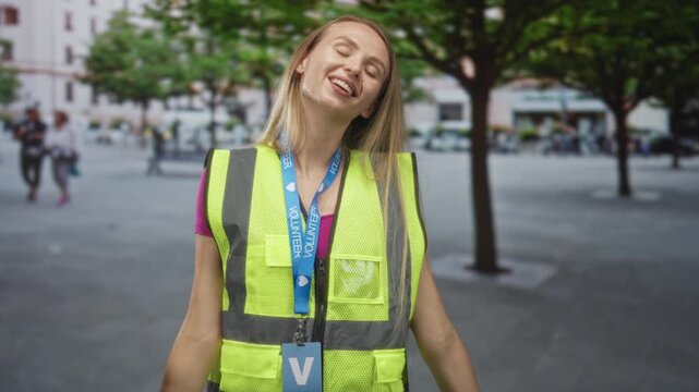 Woman in yellow reflective vest and volunteer badge smiles with closed eyes and outstretched arms on street; community service joy.