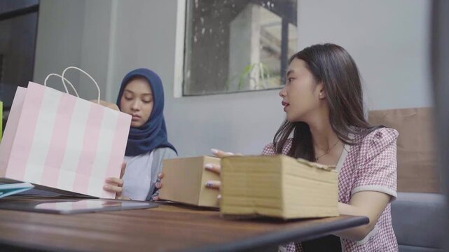 Women inspecting contents of boxes with focused attention in livingroom closeup, woman wearing hijab peers into pink bag