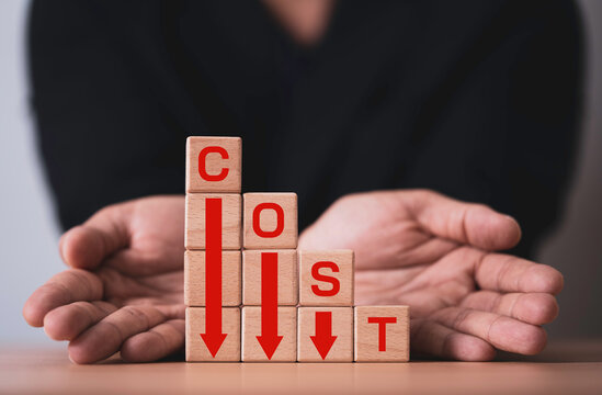 Business cost reduction concept with wooden blocks and downward arrows protected by human hands, symbolizing financial crisis management, budgeting, savings, risk control and economic decline.