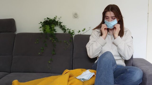 Young woman alarmed by news about dangerous new virus quickly puts on multiple medical masks trying to protect herself from possible pandemic at home