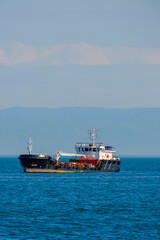 Fototapeta premium Small black and white coastal supply ship sailing against a clear sky