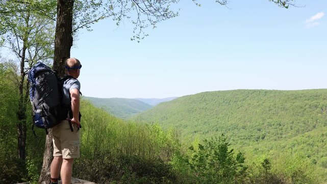 Middle-aged backpacker enjoys a scenic view from a mountaintop rocky outcrop vista