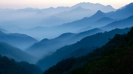 Naklejka premium Layered mountain ranges enveloped in soft morning mist create a serene and vast natural landscape