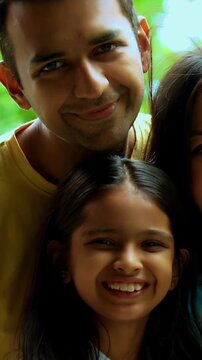 Indian parents with infant outdoors in garden, smiling while standing, looking at camera, showcasing happy family bonding, lifestyle, love, parenthood, outdoor portrait in natural greenery