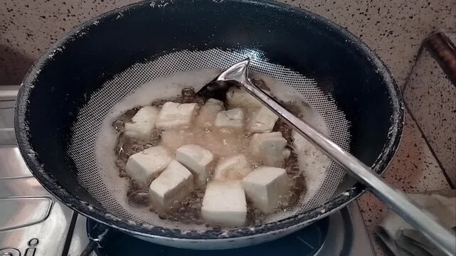 white tofu frying process in hot oil pan at home kitchen
