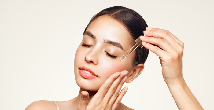 Young beautiful woman applying face serum with pipette. Cosmetic procedures for facial skin care