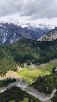 A majestic landscape view showcasing lush green alpine forests, rolling meadows, and a winding river nestled beneath dramatic, snow-capped jagged mountain peaks under cl mountain landscape in the alps