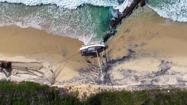 Aerial video capturing a stranded sailboat resting on the sand at Forster Beach in NSW Australia. Waves roll onto the shoreline beside the abandoned vessel