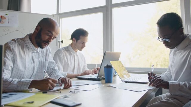 A diverse group of professionals collaborates on crypto trading strategies in a bright office setting. They use laptops and discuss plans while focusing on workplace analysis