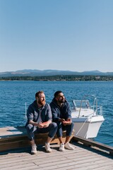 Obraz premium Two men sitting on a dock holding shells and looking at the sea for social media banner and travel background