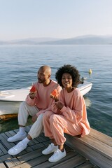 Obraz premium Couple by lake eating watermelon on dock summer lifestyle background for banner and relaxed outdoor snack scene