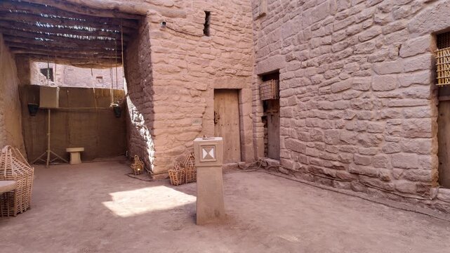 AlUla Old Town's narrow alley offering a view of ancient mud brick architecture and wooden doors under a bright blue desert sky, showcasing the historic heritage of Saudi Arabia