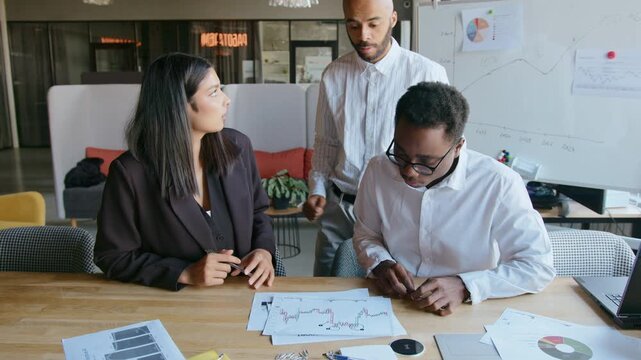 Man throws documents with graphs on table as sign of dissatisfaction with work of his team and shows where they were wrong. Twice other colleagues listen to his arguments