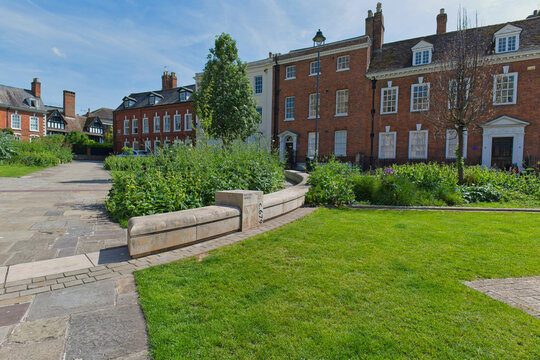 traditional brick houses with white windows, a green lawn, and bushes in the foreground in Gloucester - Gloucestershire - UK