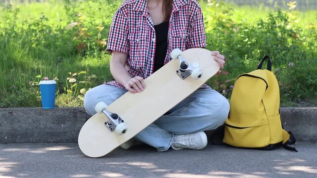 Girl spins wheels on skateboard checking their serviceability. Teenager preparing to ride, examining details of her first skateboard. Close-up of hands and skate outdoors. Skateboard inspection