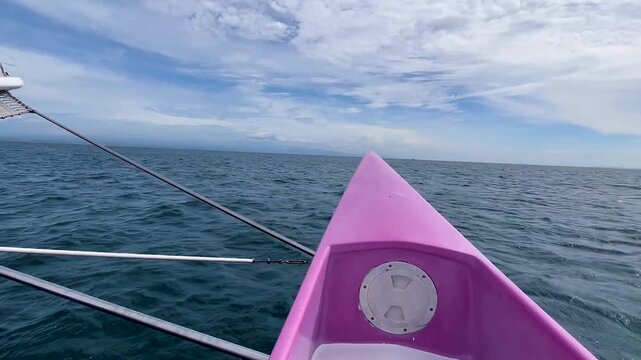 View from trimaran ama hull slicing calm sea under cloudy sky 