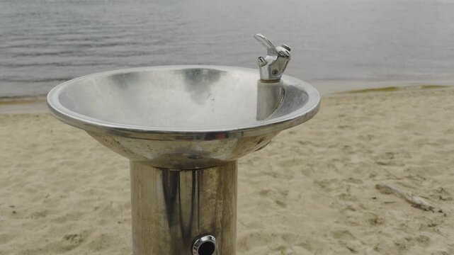 Drinking Water Fountain Standing On Sandy Beach Near River. Infrastructure Object For Fresh Water