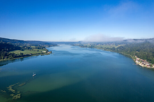 Lac jurassien vu par drone avec voile de brume et voilier solitaire