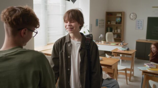 Teenage boy giving his friend fake handshake before actually shaking his hand in modern classroom before 3D modeling class
