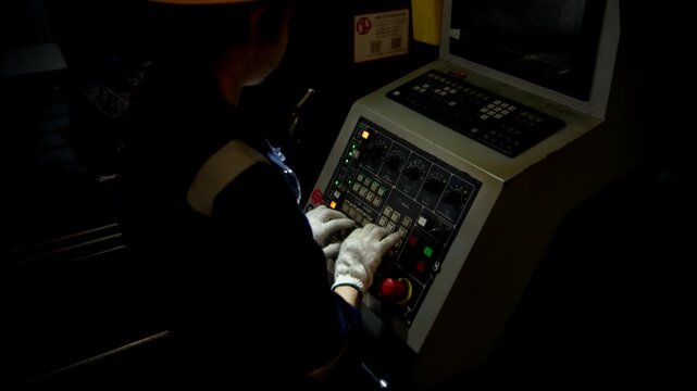 An industrial young woman technician stands in front of a control panel and overseeing the operation of machinery in a car parts manufacturing plant