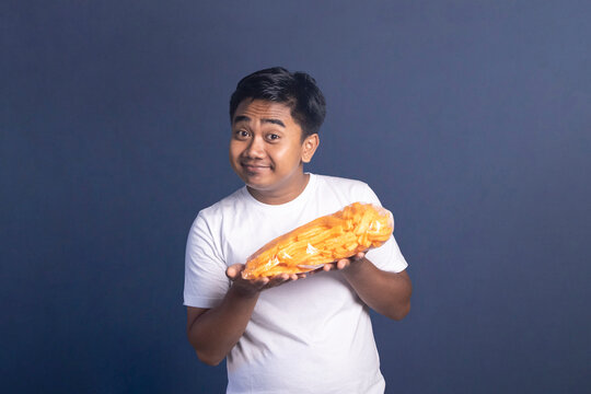 Indonesian man in white t-shirt holding a large bag of orange snacks horizontally with a smug smirk