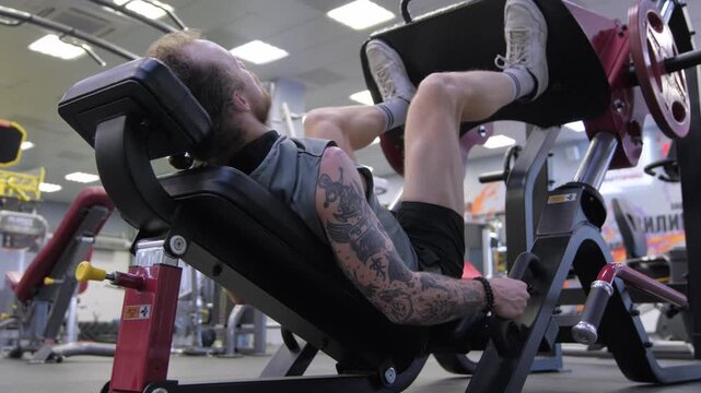 Man exercises leg press in gym during afternoon workout session