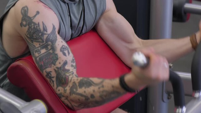 Man exercises arms at gym with focus on tattoos and workout equipment in action