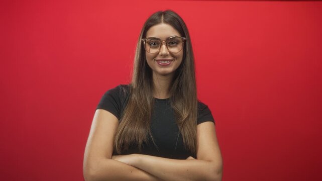 Woman with glasses crossing her arms and smiling against a red studio backdrop; confidence approachable.