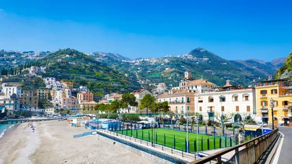 Minori Italy coastal town with hillside terraces, colorful buildings, beach and sports field under clear blue sky. Minori architecture blends with green hills creating scenic Mediterranean landscape  © IgorZh