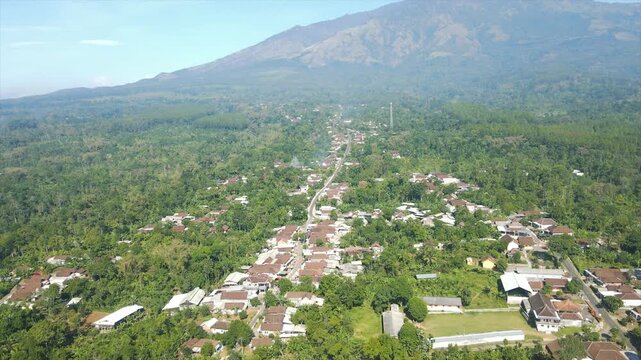 Aerial view of a beautiful Indonesian village using a drone in 4K resolution, located under a large, always bright volcano.