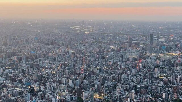 Aerial high-angle footage captures a panoramic evening view of Tokyo city from the Tokyo Skytree observation deck. The camera overlooks the winding Sumida River with its iconic bridges. 