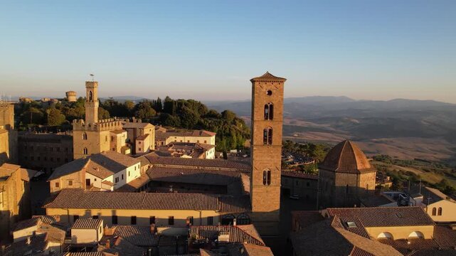 Volterra Tuscany Italy Aerial Drone Sunset Pullback Reveal Scenic View of Cathedral Bell Tower and Baptistery of San Giovanni Medieval Hilltop Townscape Architecture in Golden Earth Tones 4K UHD