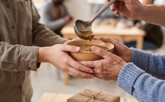 Close up of a volunteer serving hot lentil soup into a bowl held by an elderly person at a community charity event.