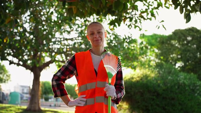 Confident female municipal worker hold rake in city park during golden hour, representing women at work, environmental responsibility, sustainability, and positive public service in urban green spaces