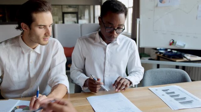 Three men work together on a contract while discussing key points. One man points out important clauses that need attention for a strong agreement
