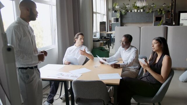 A diverse group of four people engages in a business discussion. They brainstorm ideas, share notes, and collaborate on a presentation at the office table while focusing on teamwork