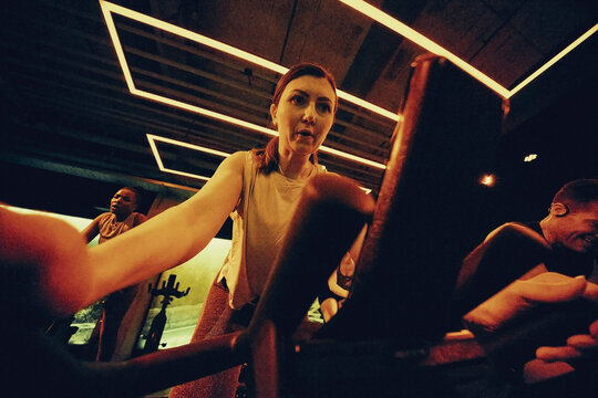 Woman leading intense indoor cycling spin class workout with diverse group in moody gym lighting